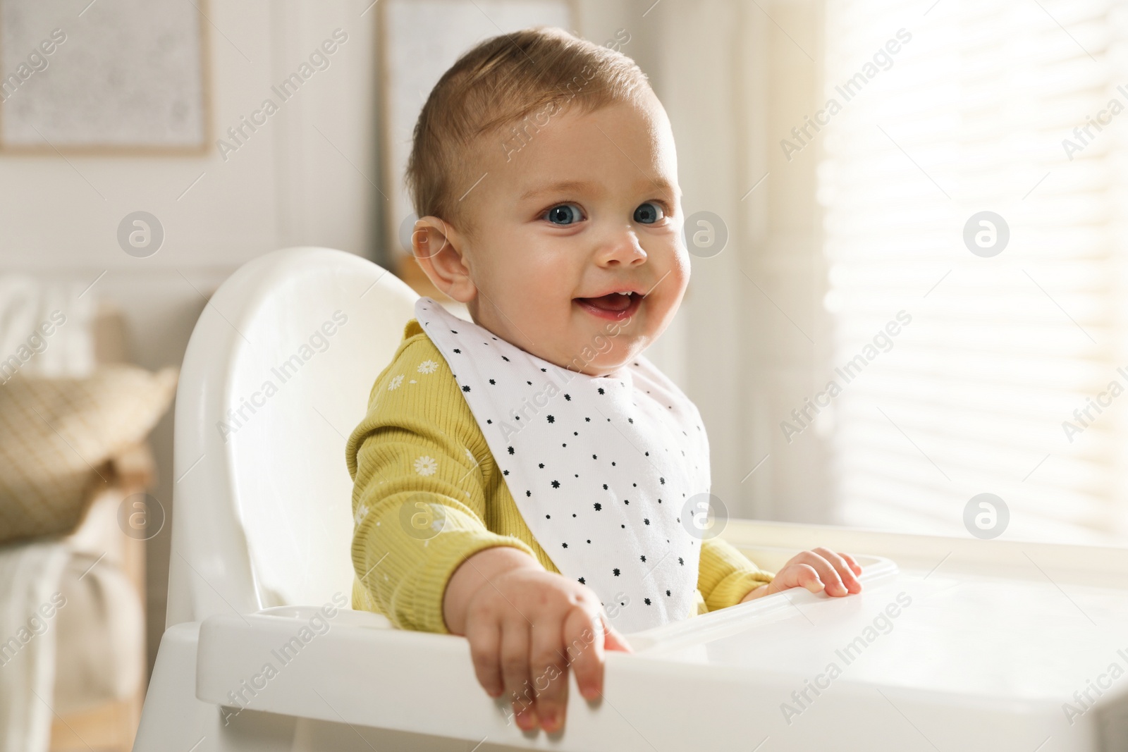 Photo of Cute little baby wearing bib in highchair at home