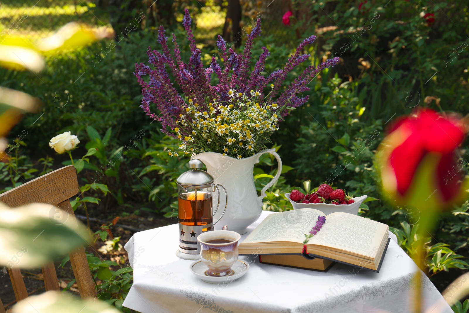 Photo of Beautiful bouquet of wildflowers and books on table served for tea drinking in garden