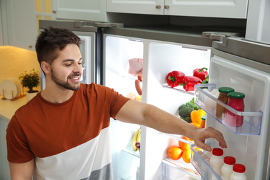 Photo of Young man taking yoghurt out of refrigerator indoors