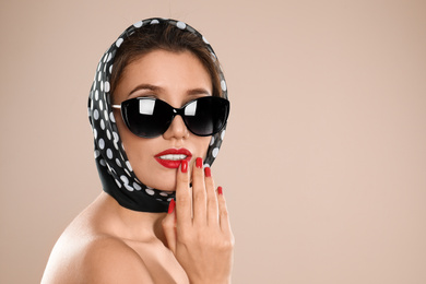 Young woman wearing stylish sunglasses and headscarf on beige background. Space for text