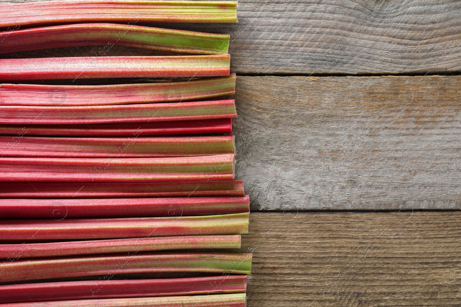 Photo of Fresh rhubarb stalks on wooden table, top view. Space for text