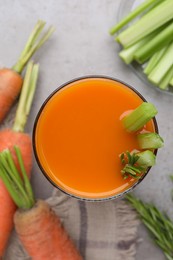Photo of Glass of tasty carrot juice with celery sticks on grey table, top view