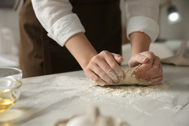 Photo of Woman kneading dough at table in kitchen, closeup