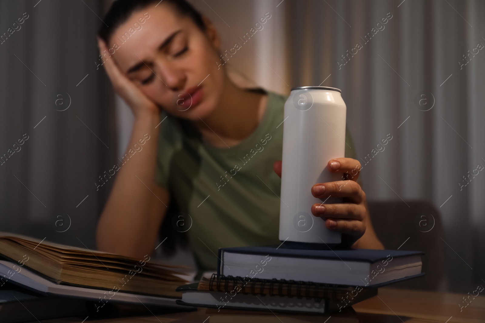 Photo of Tired young woman with energy drink studying at home, focus on hand