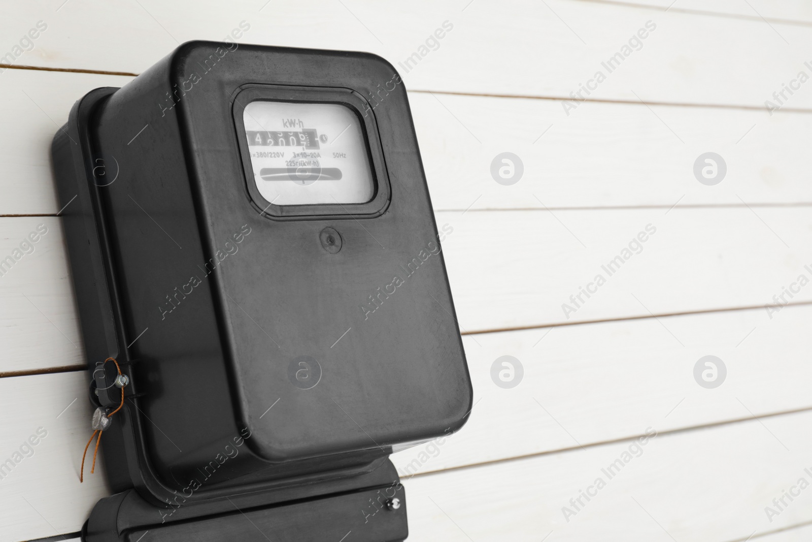 Photo of Black electric meter on white wooden wall, space for text. Measuring device