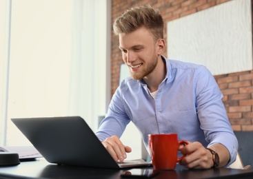 Photo of Young man using laptop at table indoors