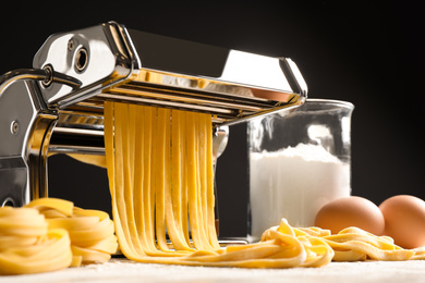 Photo of Pasta maker machine with dough and products on grey table