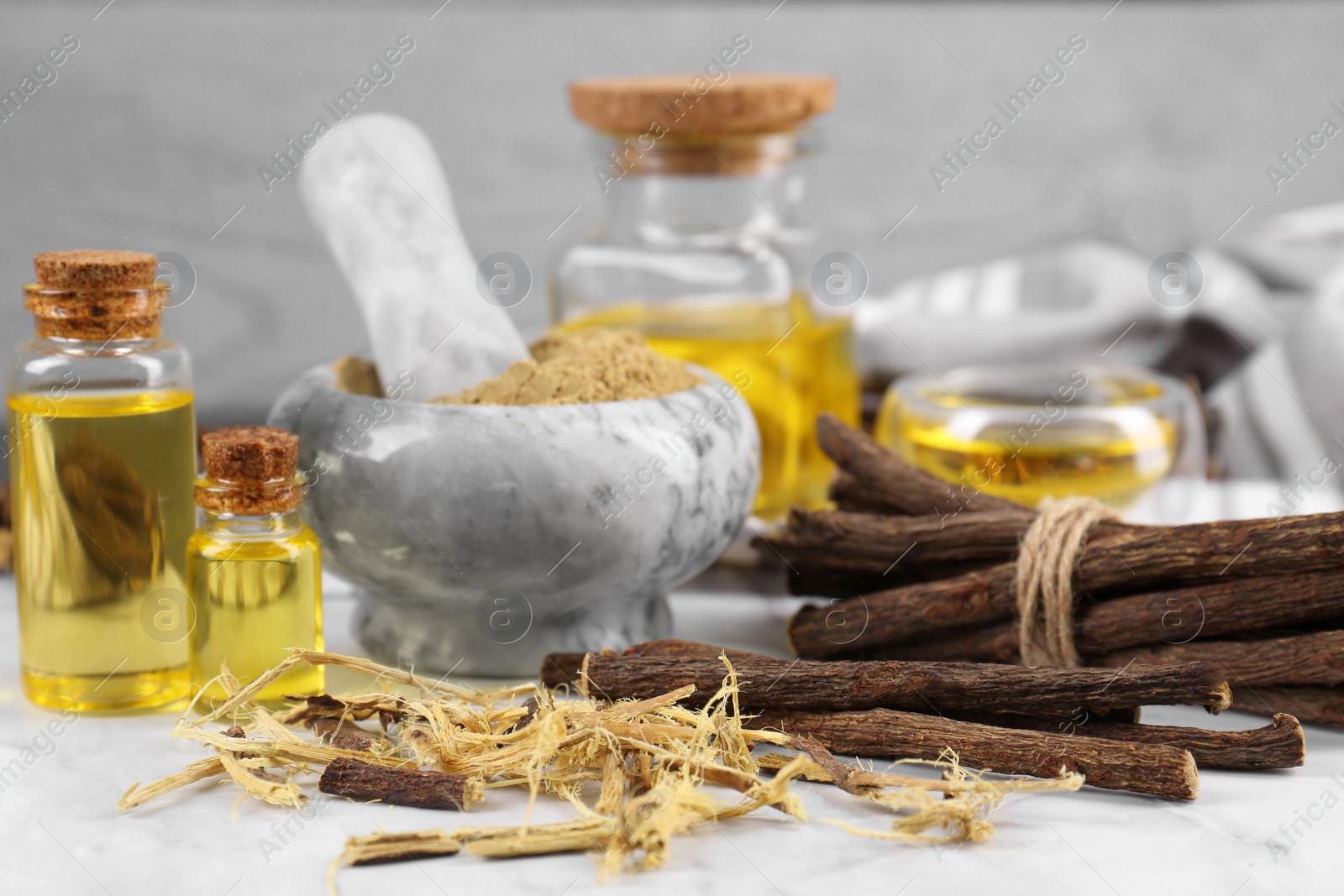 Photo of Dried sticks of licorice roots, shavings and essential oil on white table, closeup