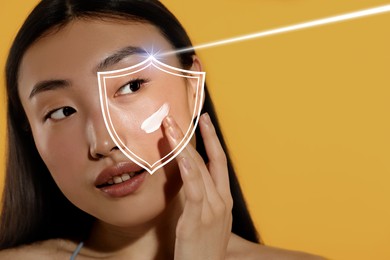 Image of Beautiful woman applying sunscreen onto face against golden background, space for text. Illustration of shield symbolizing sun protection