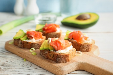 Photo of Tasty sandwiches with fresh sliced salmon fillet and avocado on wooden board, closeup