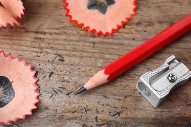 Photo of Pencil, sharpener and shavings on wooden table, closeup