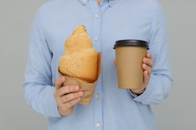 Photo of Young female intern with croissant and cup of drink on grey background, closeup