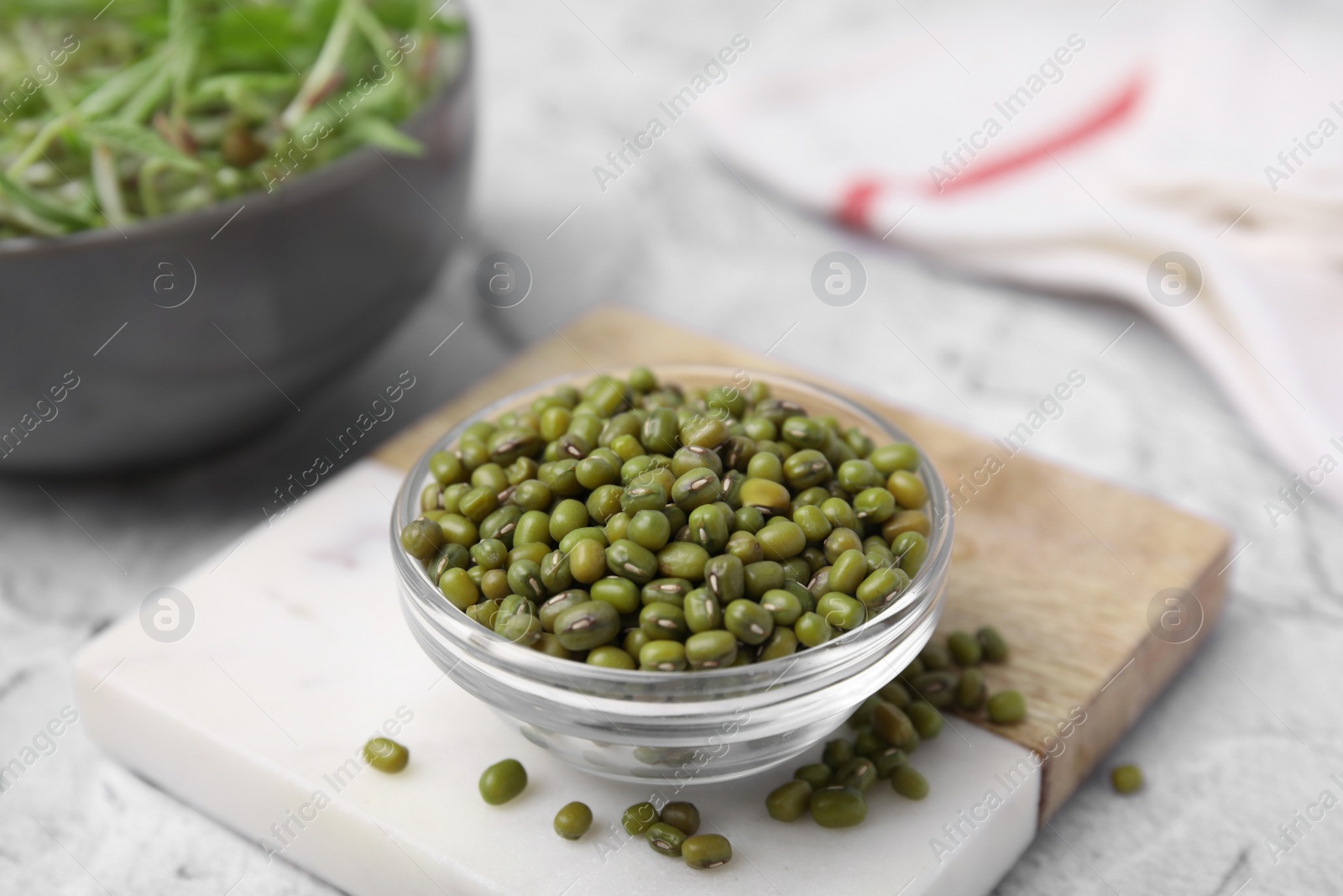 Photo of Glass bowl with mung beans and coaster on white textured table, closeup