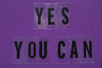 Photo of Phrase Yes You Can of plastic letters on purple background, top view. Motivational quote