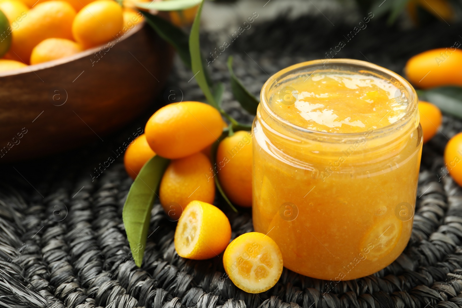 Photo of Delicious kumquat jam in jar and fresh fruits on mat, space for text