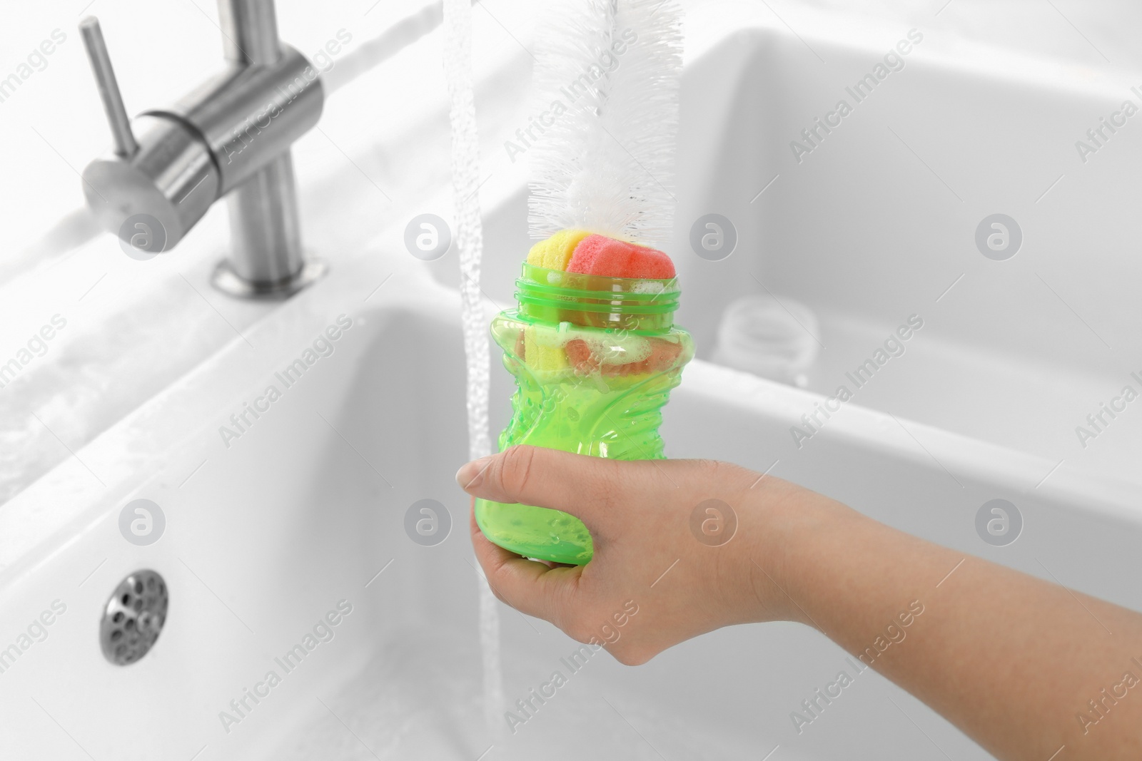 Photo of Woman washing baby bottle with brush in kitchen, closeup