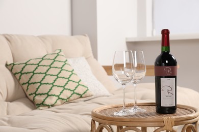 Photo of Glasses and wine on rattan table near sofa in living room. Interior design