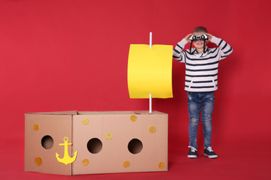 Photo of Little child playing with ship made of cardboard box on red background