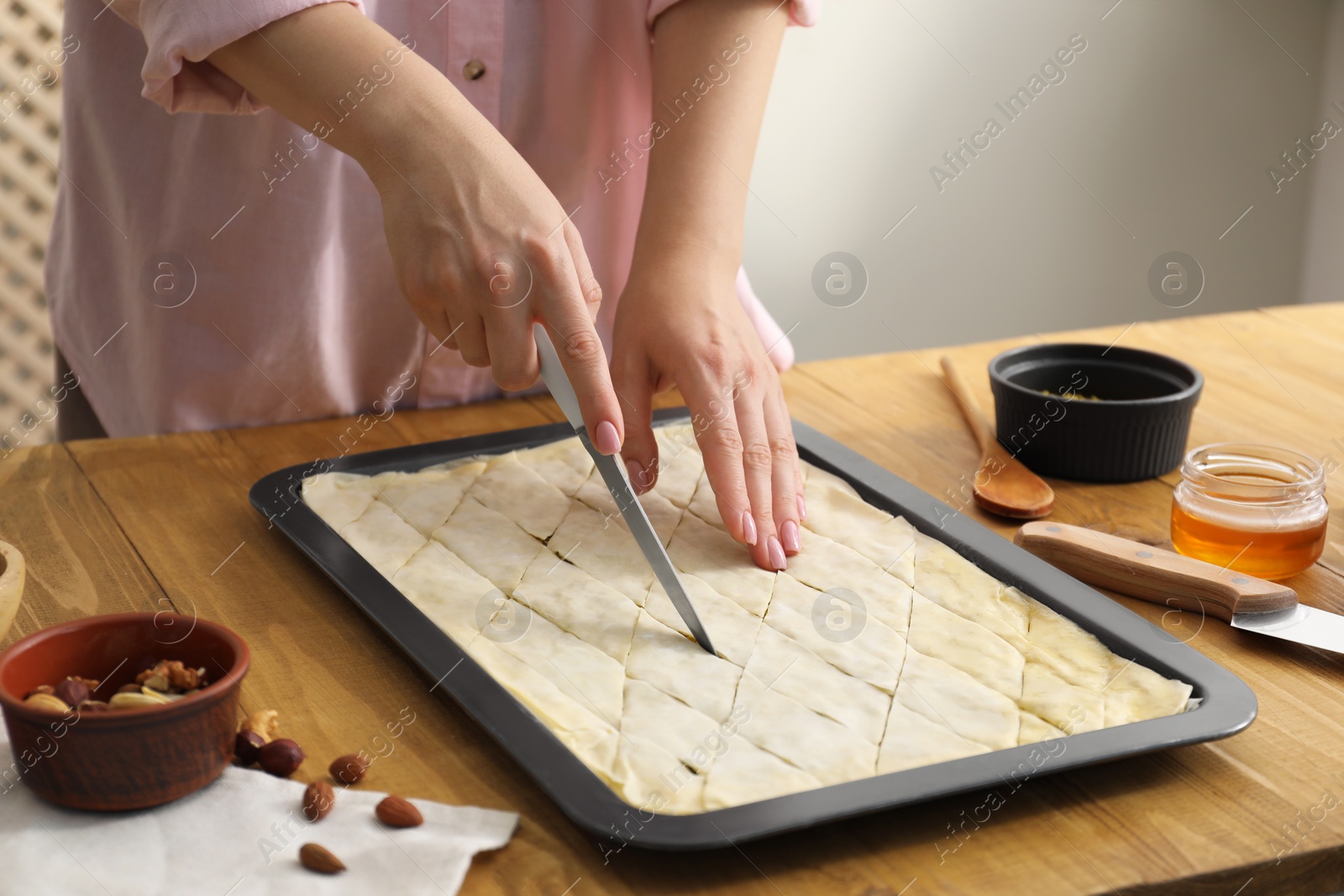 Photo of Making delicious baklava. Woman cutting dough in baking pan at wooden table, closeup