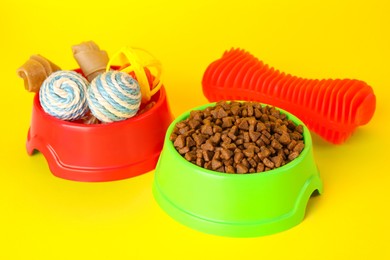 Photo of Various bright pet toys and bowl of food on yellow background
