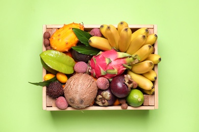 Photo of Different tropical fruits in wooden box on green background, top view