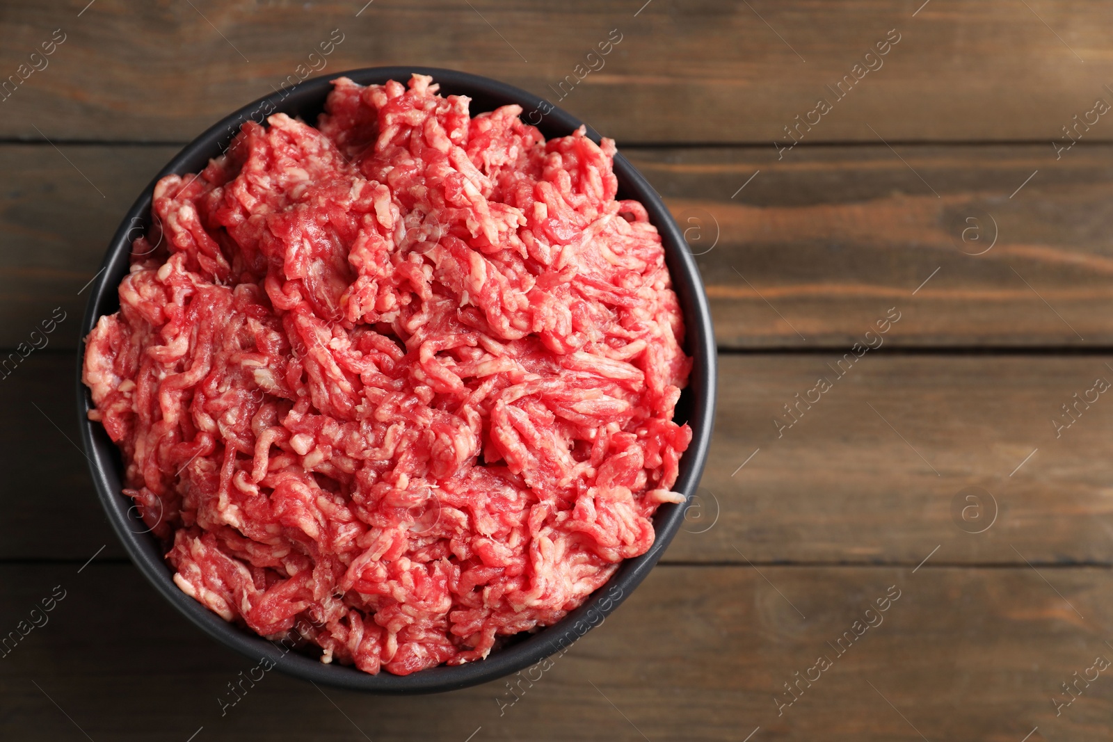 Photo of Raw ground meat in bowl on wooden table, top view. Space for text