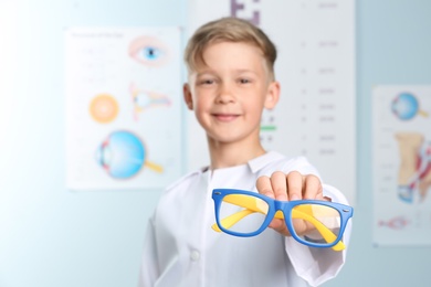 Photo of Cute little boy with eyeglasses in ophthalmologist office