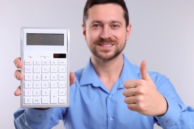 Photo of Happy accountant with calculator showing thumbs up on light grey background, selective focus