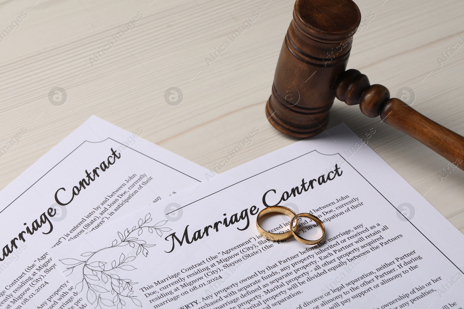 Photo of Marriage contracts, gold rings and gavel on light wooden table, closeup