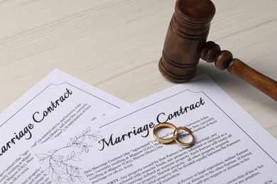 Marriage contracts, gold rings and gavel on light wooden table, closeup