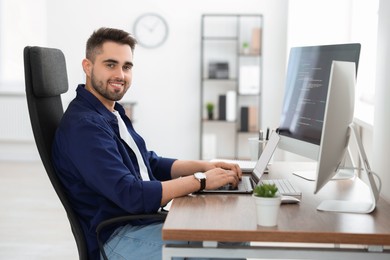 Happy young programmer working with laptop in office