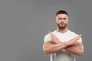 Photo of Stop gesture. Man with crossed hands on grey background, space for text