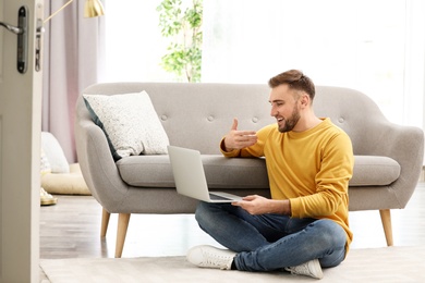 Photo of Young man using video chat on laptop in living room