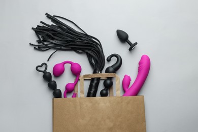 Photo of Paper shopping bag with different sex toys on white background, flat lay