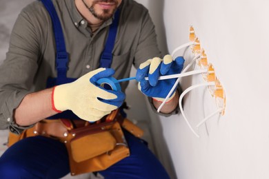 Photo of Electrician with insulating tape repairing power socket indoors, closeup