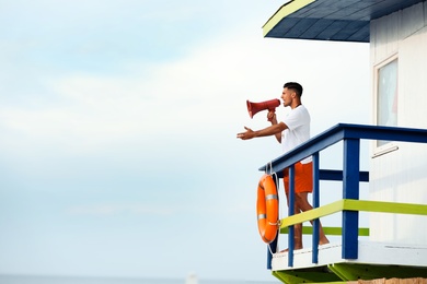 Male lifeguard with megaphone on watch tower against blue sky