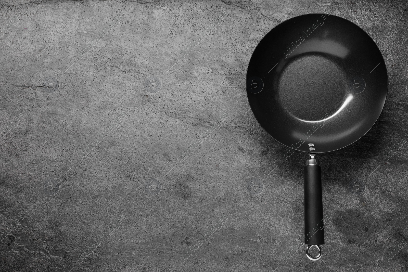 Photo of Empty iron wok on grey textured table, top view. Space for text