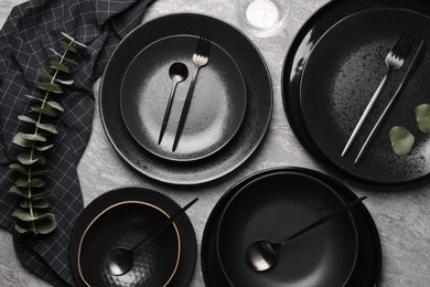 Photo of Stylish table setting. Dishes, cutlery and eucalyptus branch on grey surface, flat lay