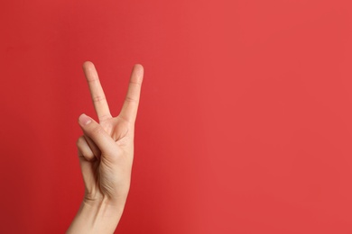 Woman showing victory sign on color background. Space for text