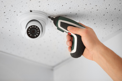 Technician installing CCTV camera on ceiling indoors, closeup