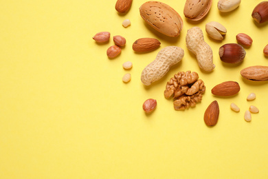 Different delicious nuts on yellow background, flat lay. Space for text