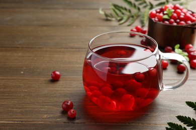 Photo of Tasty hot cranberry tea in glass and fresh berries on wooden table