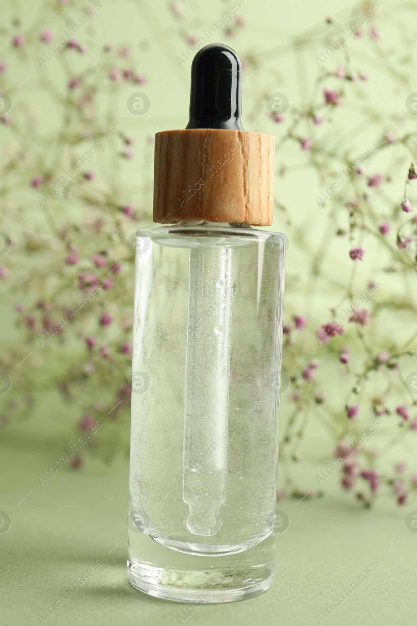 Photo of Bottle of face serum and beautiful flowers on light green background