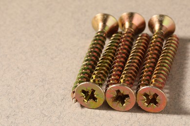 Many metal screws on beige background, closeup. Space for text