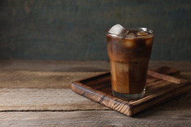 Glass of delicious iced coffee with milk on wooden table, space for text