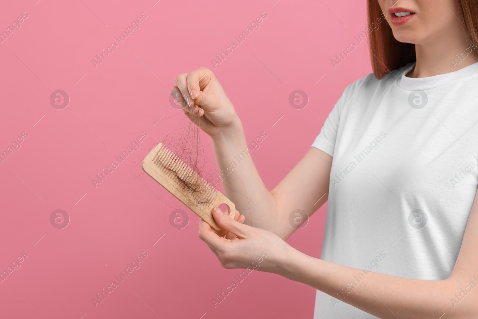 Photo of Woman untangling her lost hair from comb on pink background, closeup and space for text. Alopecia problem