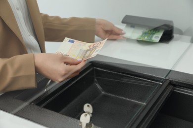 Photo of Cashier checking money with currency detector at exchange department, closeup