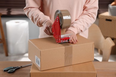 Photo of Seller taping parcel at table in office, closeup