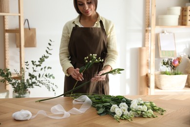 Photo of Florist making beautiful bouquet at table in workshop, closeup