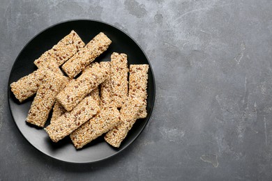 Plate with tasty sesame seed bars on grey table, top view. Space for text